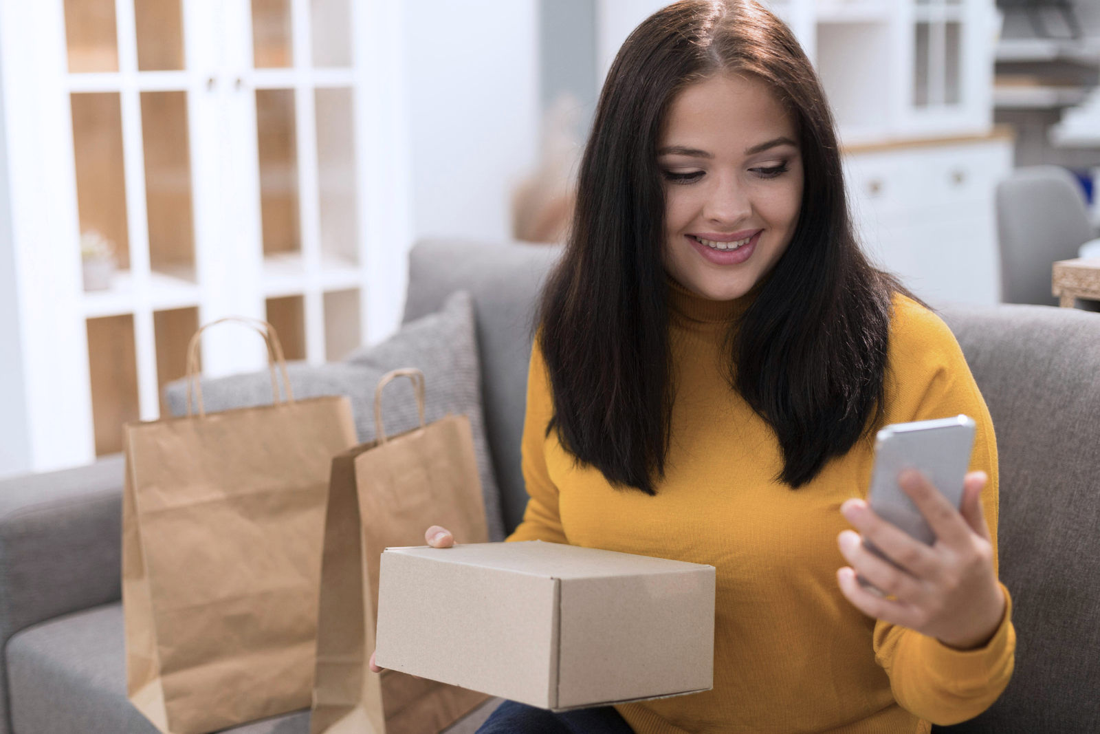Mulher, sentada no sofá, fazendo compras no e-commerce utilizando o celular