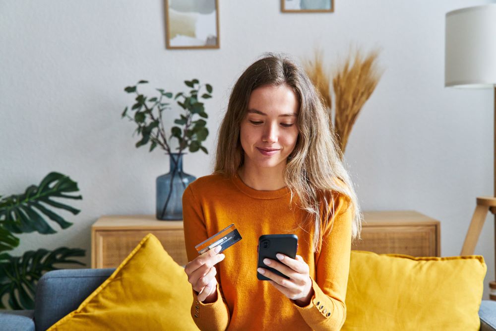 Menina loira zillennial faz compra omnichannel com um cartão e um celular na mão
